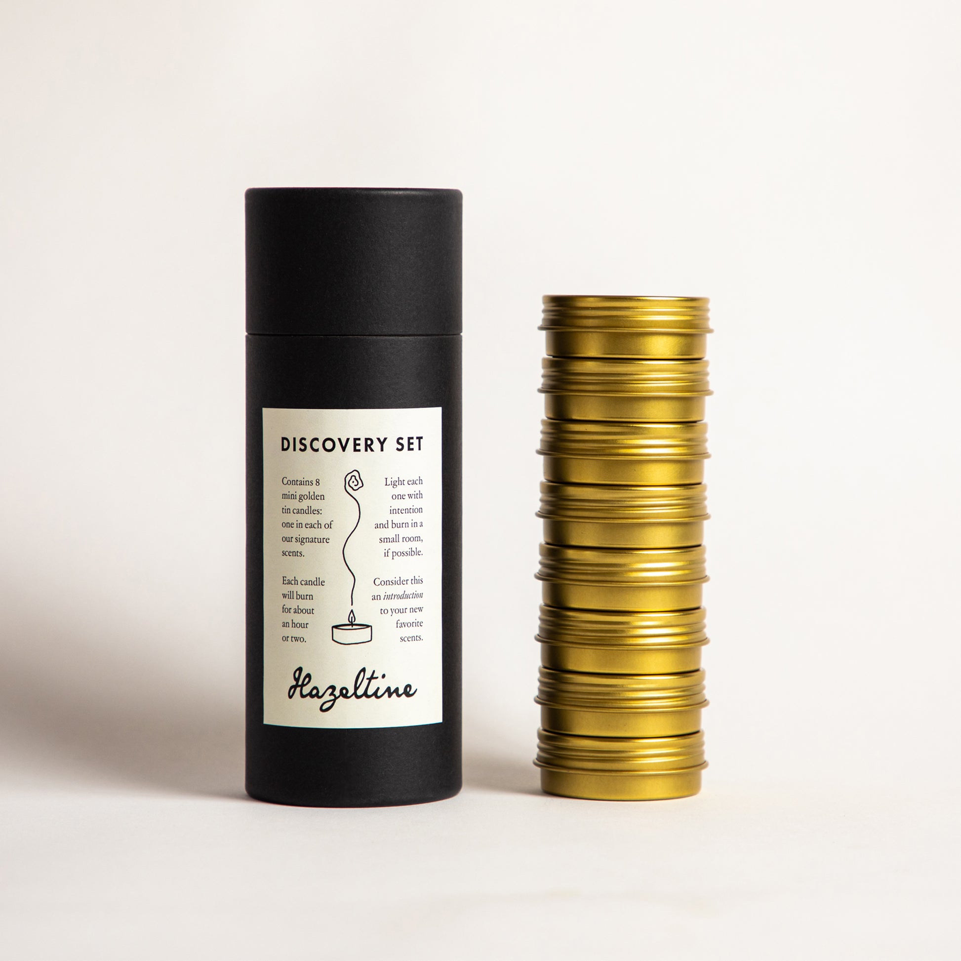 Hazeltine Discovery Set with black cylindrical box and a stacked tower of golden mini candle tins.